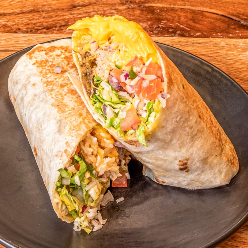 Two Dos Fuentes burritos, one cut open to show rice, lettuce, tomato, and meat filling.