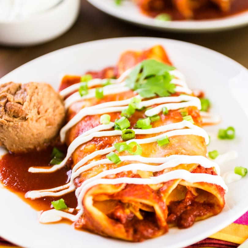 Dos Fuentes enchiladas with red sauce, sour cream, green onions, cilantro, and refried beans.